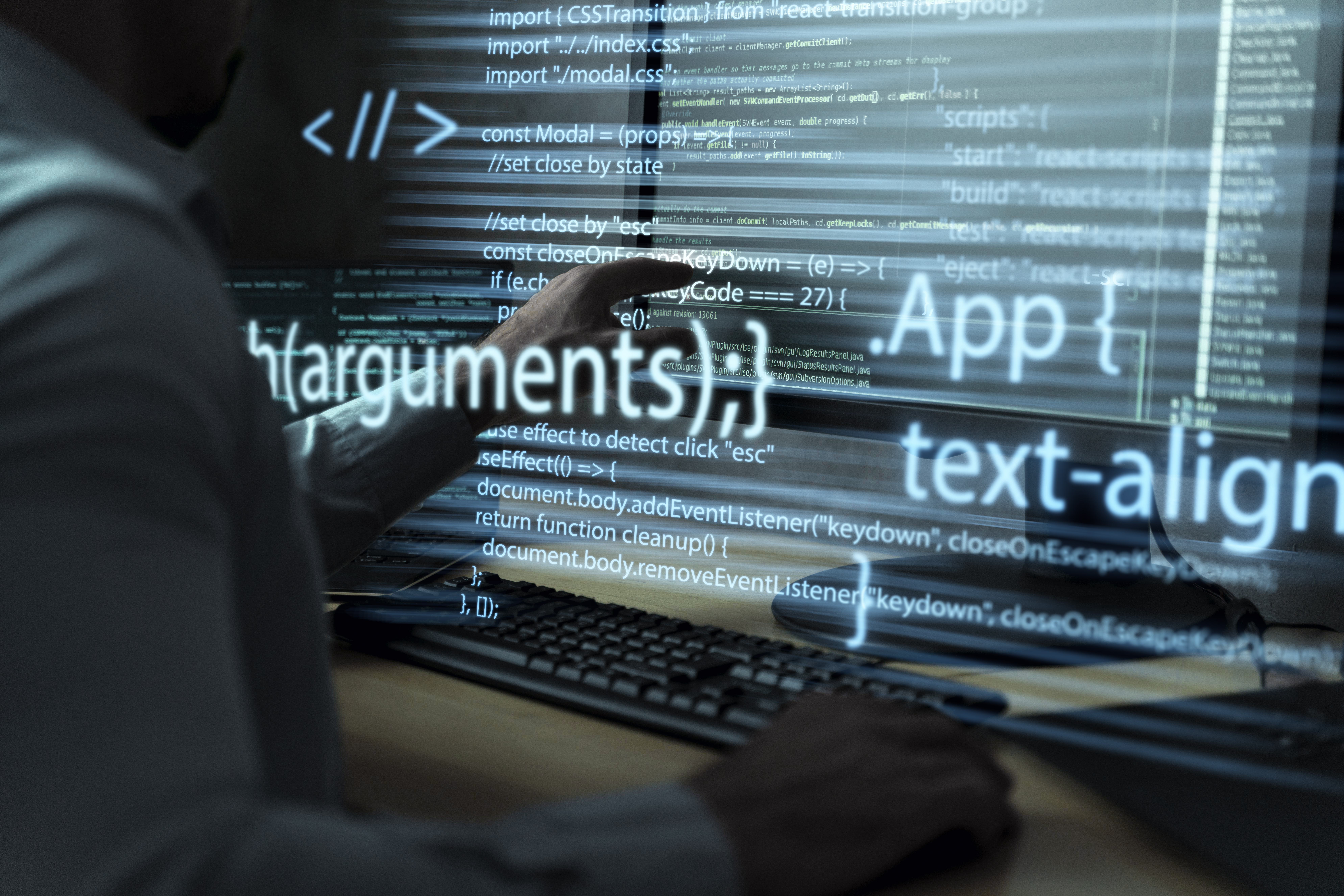 A software engineer working at a computer while application code is projected across the screen.